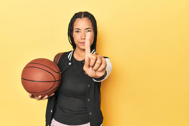 Estudante indonésia com basquete no amarelo mostrando o número um com o dedo. - Foto, Imagem