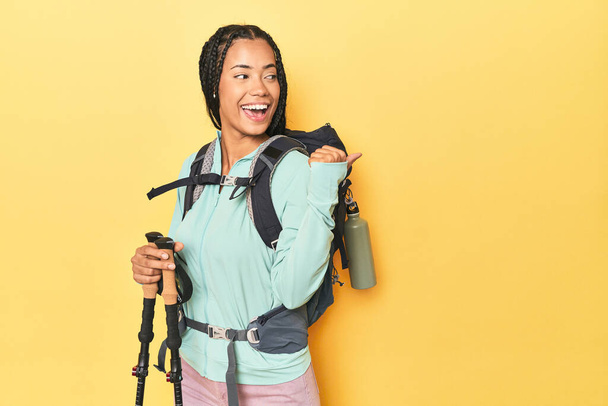 Indonesian woman with hiking gear on yellow points with thumb finger away, laughing and carefree. - Photo, Image