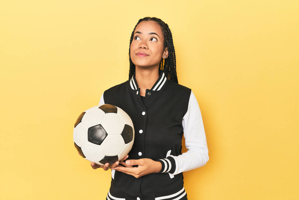 Indonéská školačka s fotbalovým míčem na žluté snění o dosažení cílů a účelů - Fotografie, Obrázek