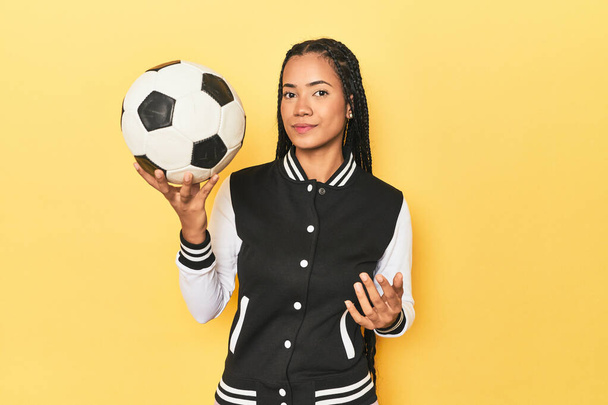 Young Indonesian woman with medal and soccer ball on yellow studio background - Photo, Image