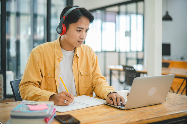 Młody azjatycki student pracujący i uczący się na laptopie w kawiarni. Wyszukiwanie wiedzy online. - Zdjęcie, obraz