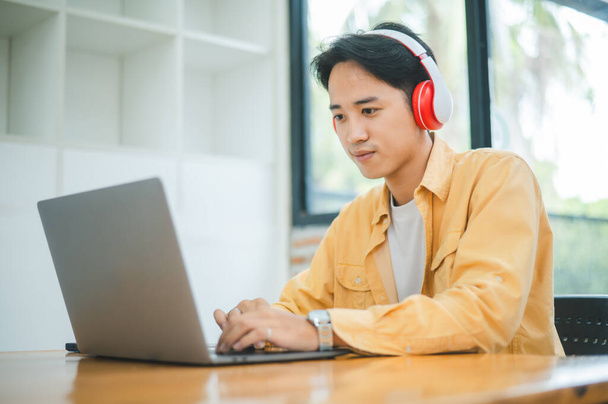 Opiskelija käyttää kannettavaa tietokonetta kahvilassa kuulokkeita käyttäessään, oppii ja etsii Internetistä ja tekee videopuhelun. - Valokuva, kuva