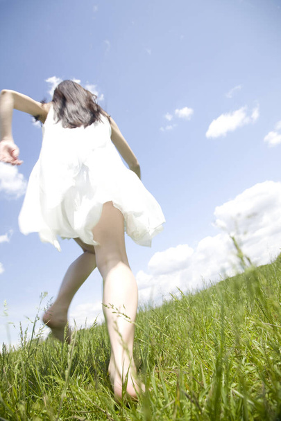 low angle view of beautiful young woman running on green grass - 写真・画像