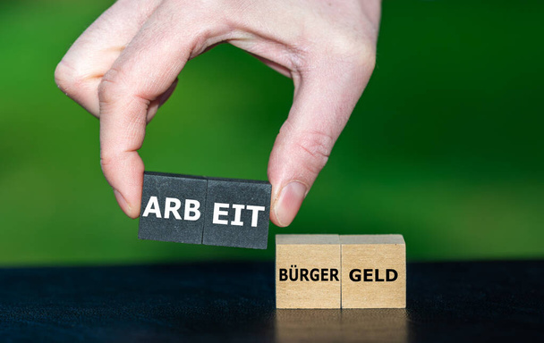 Symbol dyskusji w Niemczech, jeśli otrzymasz więcej pieniędzy z opieki społecznej w porównaniu do dochodów z pracy. i wybiera kostki ze słowem "Arbeit" (praca) zamiast "Buergergeld" (opieka społeczna) - Zdjęcie, obraz