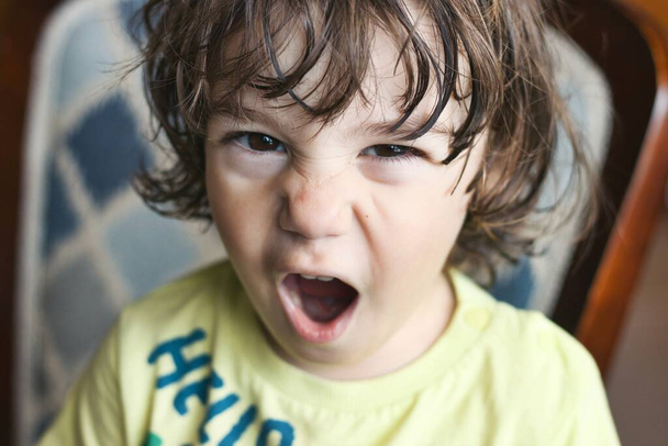Primo piano ritratto della testa di un giovane bianco ragazzo caucasico che lancia un capriccio temperamento, guardando direttamente la fotocamera con un'espressione arrabbiata sul suo viso - Foto, immagini