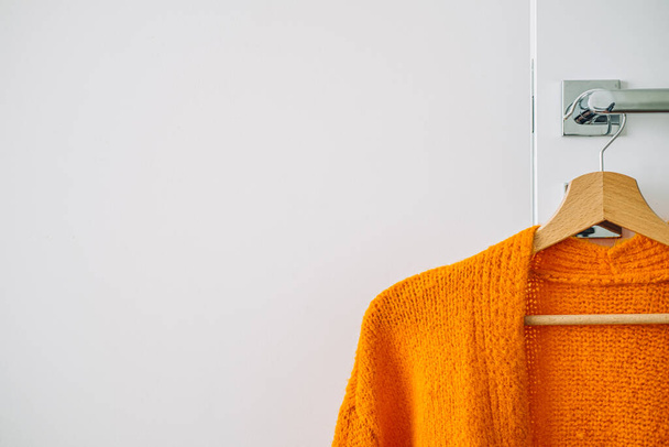 Осенью осенью минималистский гардероб с оранжевым теплым вязаным свитером на деревянной вешалке. Осенняя капсула, тёплые модные тенденции и стильный тёплый фон, трикотаж, пространство для копирования - Фото, изображение