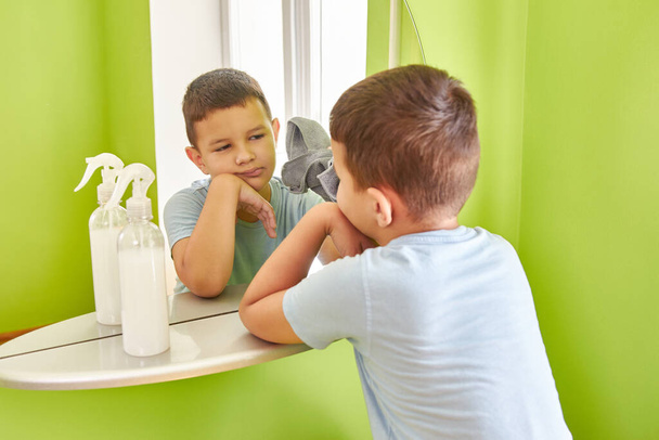 Poika pesee peilin rätillä ja pesuaineella. Läksyjä. Talon siivous. - Valokuva, kuva