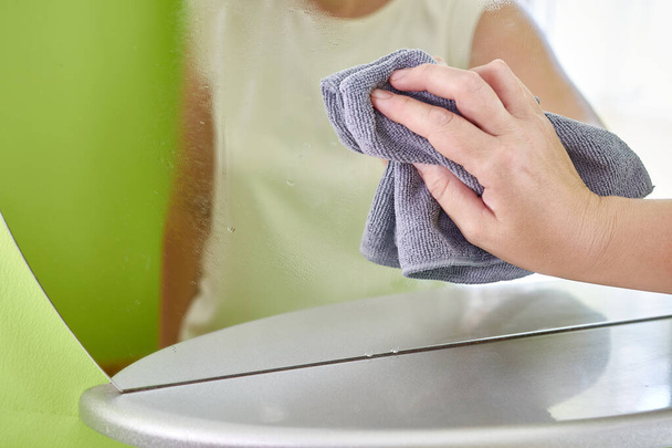 Μια γυναίκα πλένει έναν καθρέφτη με ένα πανί και απορρυπαντικό. Εργασία. Καθαρισμός σπιτιού. - Φωτογραφία, εικόνα