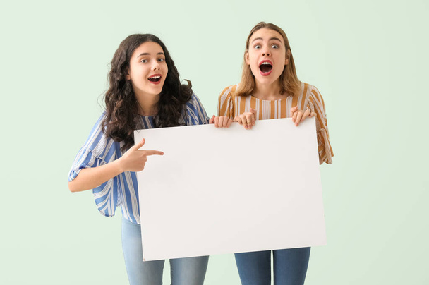 Überraschte junge Frauen mit großem leeren Plakat auf mintfarbenem Hintergrund - Foto, Bild