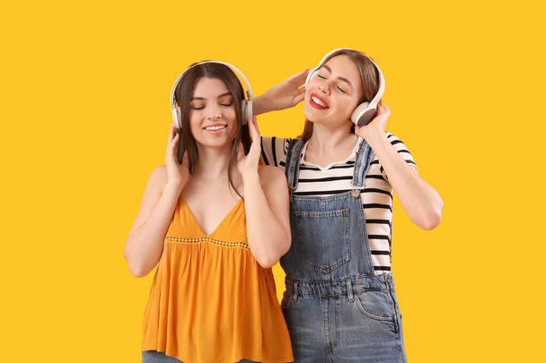 Amigos femeninos en auriculares sobre fondo amarillo - Foto, imagen