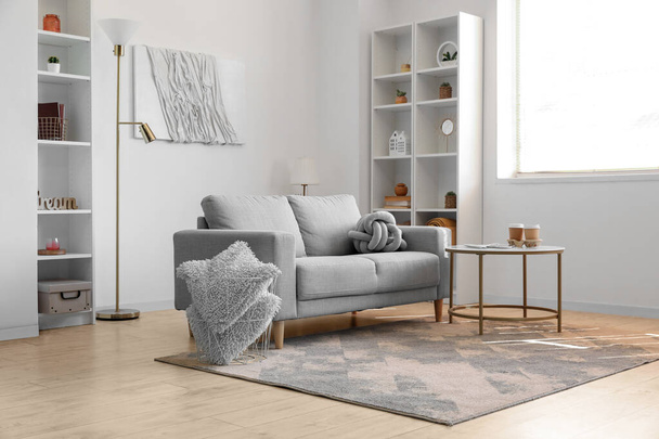 Interno di soggiorno luminoso con divano grigio, tavolo e scaffali - Foto, immagini