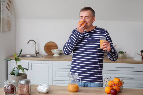 Volwassen man met glas sap en sinaasappel in keuken - Foto, afbeelding