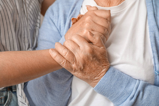 Young woman with her grandmother holding hands at home, closeup - Photo, Image