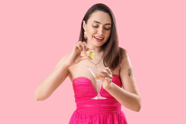 Belle femme serrant du jus de citron vert dans un verre de martini sur fond rose - Photo, image