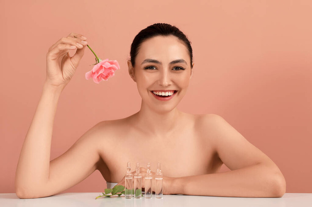 Hermosa joven con rosa y ampollas en la mesa sobre fondo rosa - Foto, Imagen
