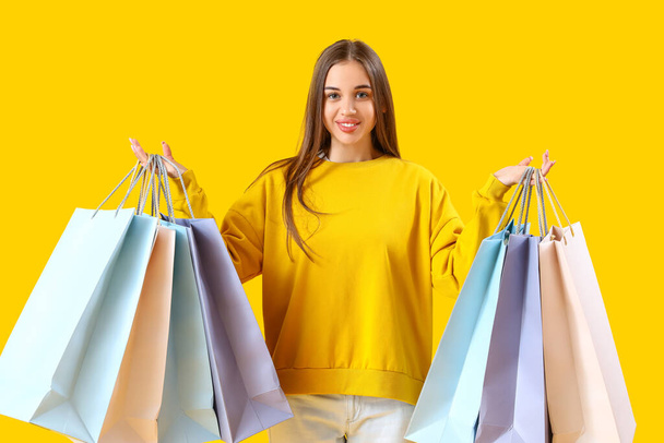 νεαρή γυναίκα με τσάντες για ψώνια σε κίτρινο φόντο - Φωτογραφία, εικόνα