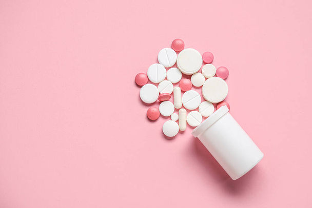 Tarro con píldoras dispersas sobre fondo rosa - Foto, imagen