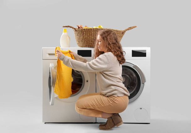 Young woman with washing machines doing laundry on light background - Photo, Image