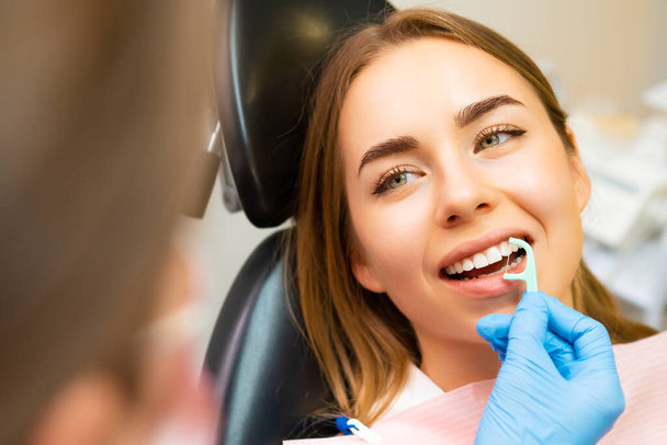 Junge schöne Frau in der Zahnarztpraxis, hört dem Arzt zu, wie man Zahnseide verwendet.  - Foto, Bild