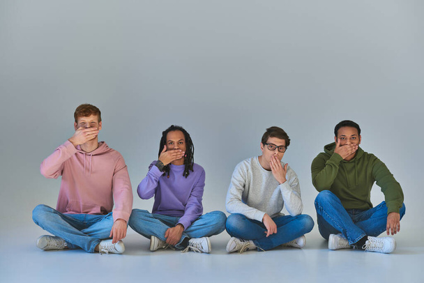 τέσσερις πολυπολιτισμικούς φίλους που κάθονται με σταυρωμένα πόδια και καλύπτουν το στόμα, πολιτιστική πολυμορφία - Φωτογραφία, εικόνα