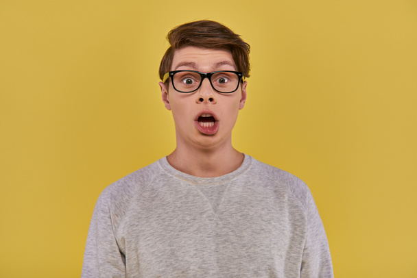 überraschter junger Mann in lässiger bequemer Kleidung und Brille blickt mit offenem Mund in die Kamera - Foto, Bild