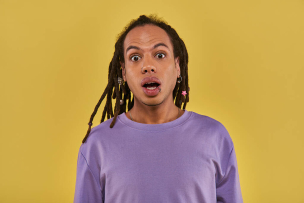 close up surprised man in purple sweatshirt with pierced lip and dreadlocks on yellow background - Photo, Image