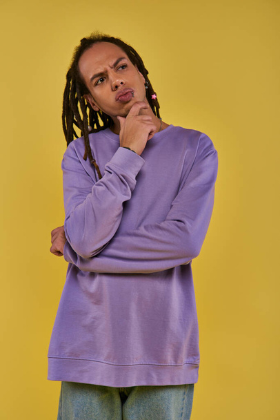 doordachte jonge man in paarse sweater denken en kijken omhoog en weg op gele achtergrond - Foto, afbeelding