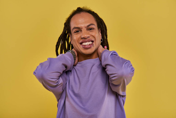 cheerful african american man with dreadlocks and pierced lip touching his neck smiling sincerely - Photo, Image