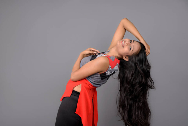 Στιγμιότυπο ενός νέου, όμορφου Ινδικού γυναικείου μοντέλου με casual φόρεμα που φοράει κόκκινο και γκρι μπλουζάκι σχεδιαστή και μπλε τζιν σε γκρι φόντο. Γυναικείο μοντέλο. Πορτρέτο μόδας. - Φωτογραφία, εικόνα