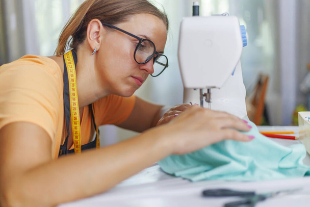 Dámské švadleny v brýlích pracuje na šicím stroji na svém pracovišti v dílně - Fotografie, Obrázek