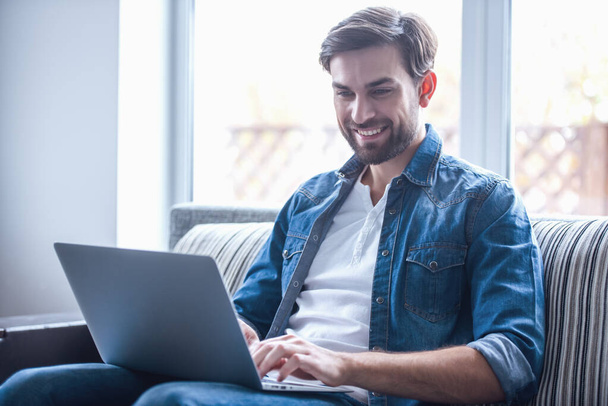Красивий бізнесмен посміхається під час роботи з ноутбуком вдома
 - Фото, зображення