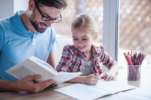 schöner Vater und seine süße kleine Tochter lesen ein Buch, zeichnen und lächeln, während sie Zeit miteinander verbringen - Foto, Bild