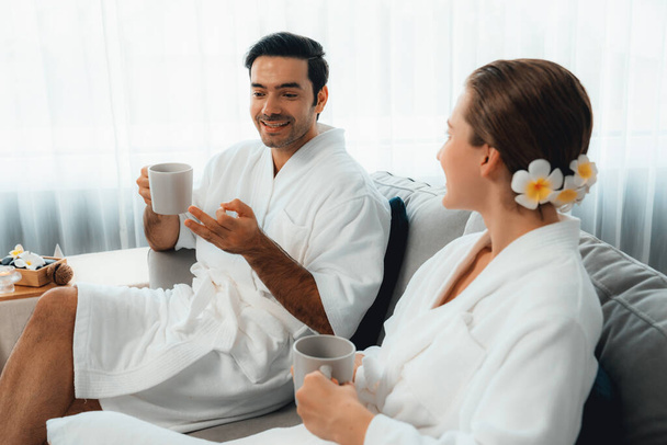 Beauty or body treatment spa salon vacation lifestyle concept with couple wearing bathrobe relaxing with drinks in luxurious hotel spa or resort room. Vacation and leisure relaxation. Quiescent - Photo, Image