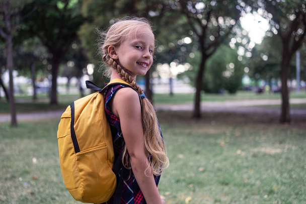 Koulutyttö mekossaan ja keltainen reppu yllään iloinen hymy, kun hän lähtee kouluun, huokuu onnea muotokuvassaan..  - Valokuva, kuva