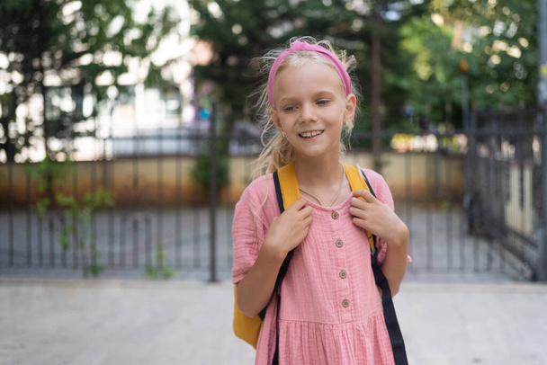 Basisschool achtergrond voor de barbie roze geklede junior schoolmeisje met een gele rugzak.  - Foto, afbeelding
