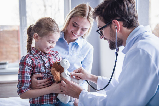 Güzel genç anne ve çocuk doktoru, küçük kızı. Doktor biraz sabırlı bir stetoskop kullanarak incelenmesi - Fotoğraf, Görsel