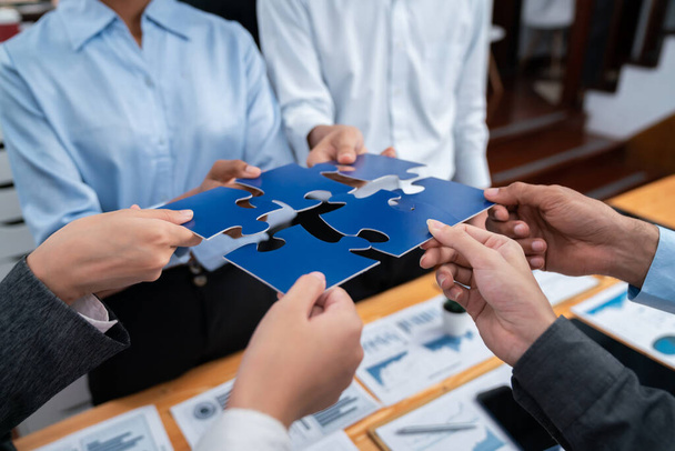 Corporate officer worker collaborate in office, connecting puzzle pieces with report paper on table as partnership and teamwork. Unity and synergy in business concept by merging jigsaw puzzle. Concord - Photo, Image