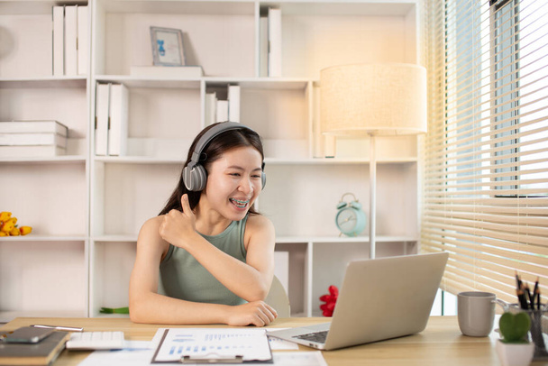 Mujer asiática joven saluda a sus amigos o colega en un video en vivo con una sonrisa en la cara, Comunicación en línea, llamada Vdo a través de computadora portátil, distanciamiento social, aprendizaje en Internet. - Foto, Imagen