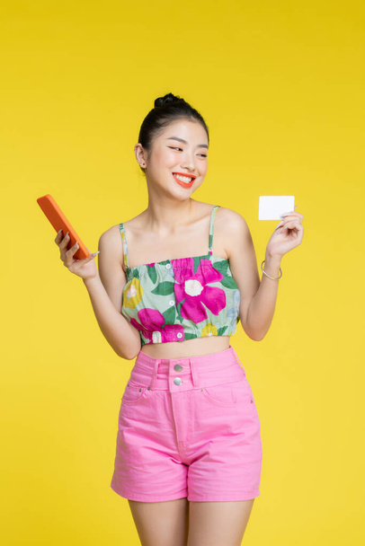 Joven mujer de Asia usando teléfono y tarjeta bancaria de crédito con expresión positiva - Foto, imagen