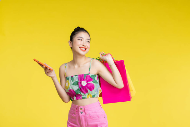 Magabiztos divatos fiatal ázsiai nő szexi ruha gazdaság színes bevásárló táskák és okostelefon - Fotó, kép