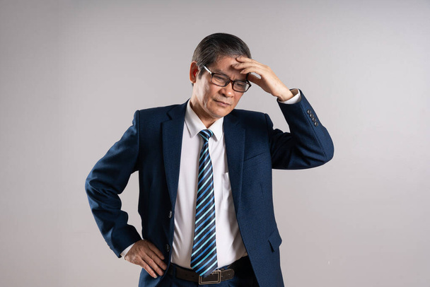 Portret van een oudere Aziatische zakenman, poserend op een blauwe achtergrond - Foto, afbeelding