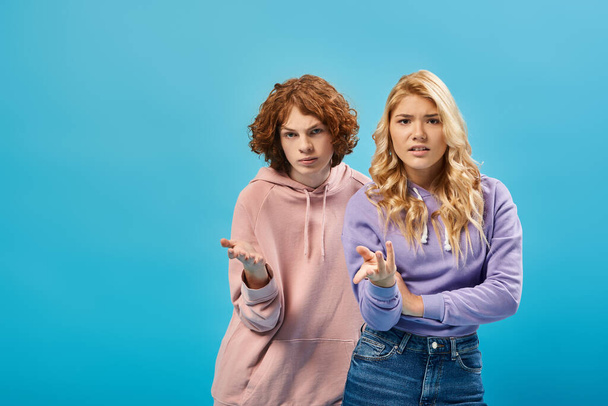 displeased teenage boy and girl in stylish hoodies pointing with hands and looking at camera on blue - Φωτογραφία, εικόνα