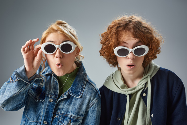 εκθαμβωτικά εφηβικά μοντέλα ποζάρουν σε κομψά γυαλιά ηλίου και κοιτάζοντας την κάμερα σε γκρι, εφηβική μόδα - Φωτογραφία, εικόνα