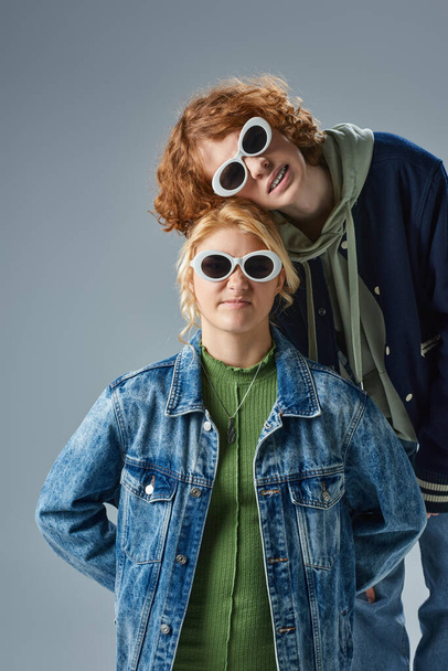 εφηβικοί φίλοι με κομψά casual ρούχα και γυαλιά ηλίου κοιτάζοντας την κάμερα ενώ ποζάρουν σε γκρι - Φωτογραφία, εικόνα