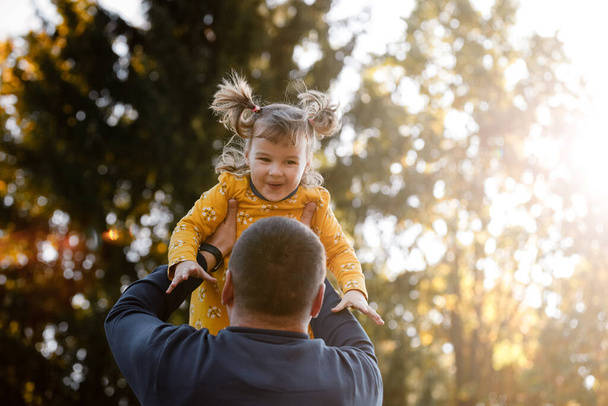 Happy fathers day. Joyful dad throws up his little smiling daughter at autumn park. Single daddy and child have fun, laugh and enjoy nature. Concept of parental care and happy carefree childhood. - Photo, Image