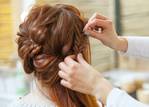 Schöne, rothaarige Mädchen mit langen Haaren, Friseur webt einen französischen Zopf, in einem Schönheitssalon. Professionelle Haarpflege und Frisurengestaltung. - Foto, Bild