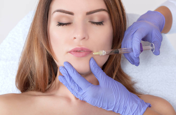 Лікар-косметолог робить процедуру збільшення губ красивою жінкою в салоні краси. Косметологія догляд за шкірою
. - Фото, зображення