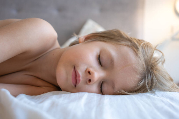 子供は顔を閉じて眠る。子供は昼寝をする。ベッドで寝てる子供。寝室の快適なマットレス。柔らかい枕、快適で居心地の良い快適なベッドコンセプト。健康な子供たちが寝て. - 写真・画像