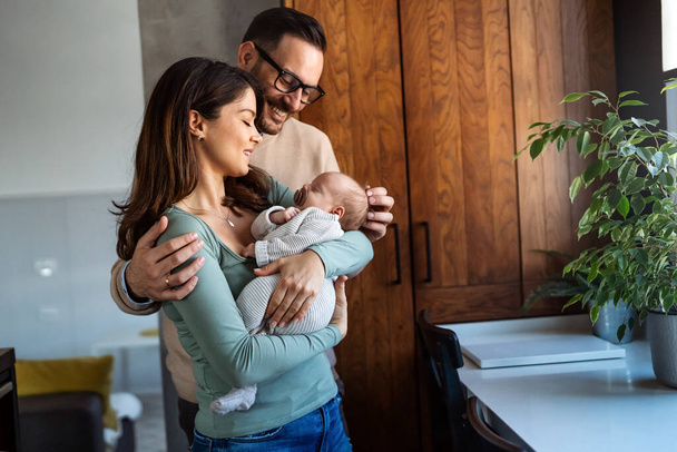 Portrait of young happy man and woman holding newborn cute babe dressed in white unisex clothing. Caucasian smiling father and mother embracing tenderly adorable new born child. Happy family concept - Foto, imagen