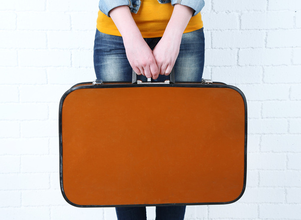 Woman holding old suitcase on brick wall background - Fotoğraf, Görsel